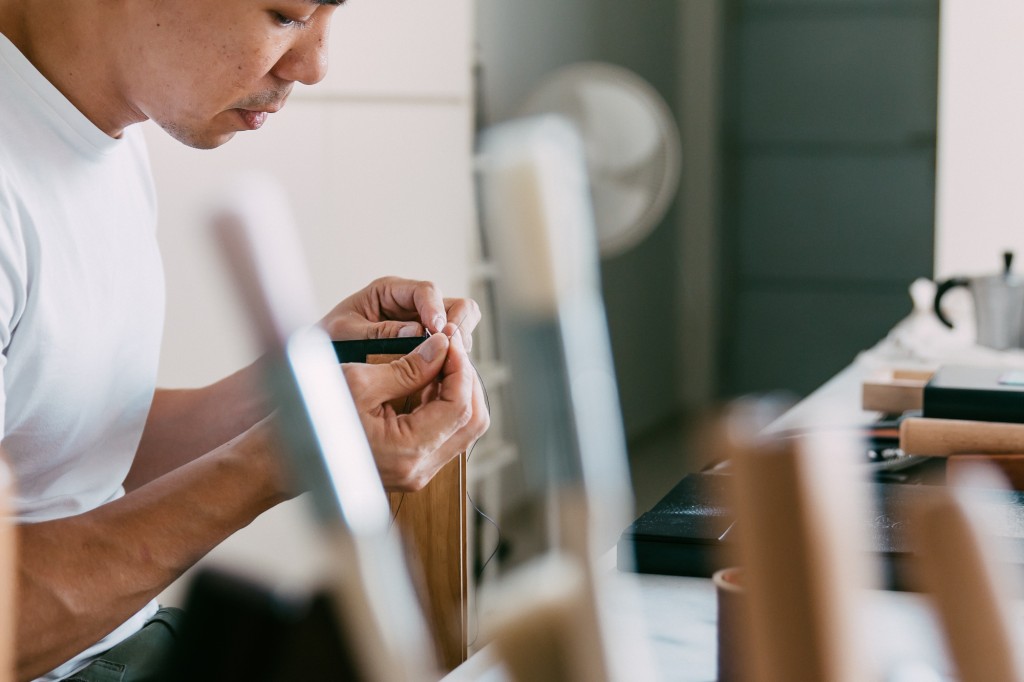 Using traditional handcrafting techniques, the leather is held together using a wooden clamp, while the crafter performs each stitch with precision